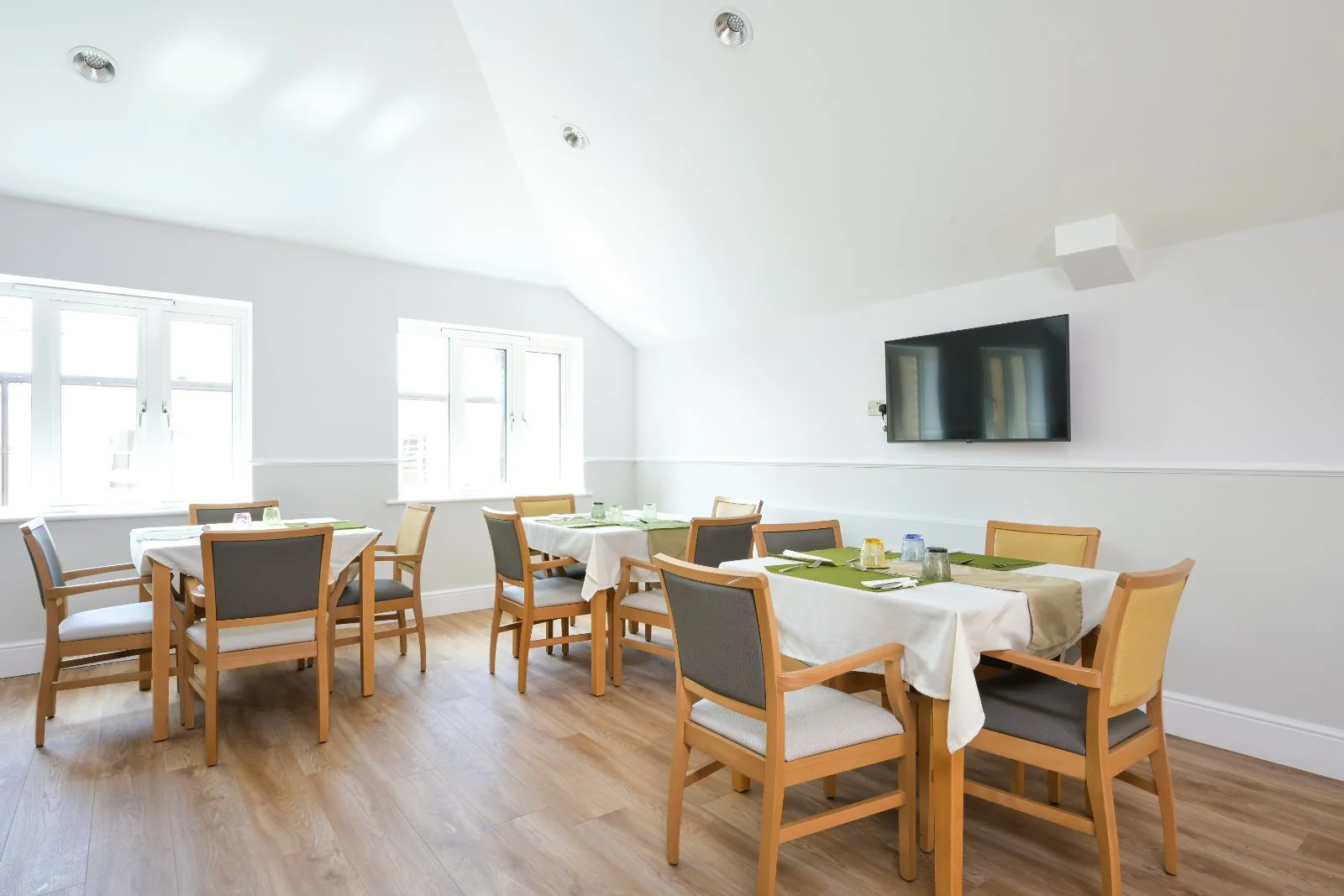 Dining room with wooden chairs and tables laid with green placemats