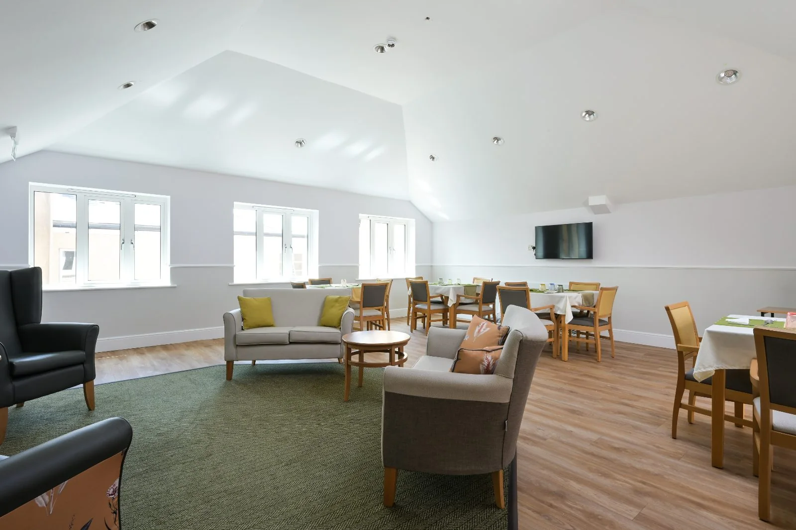 Lounge with sofa, armchairs and a green rug under a vaulted ceiling